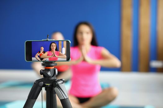 Camera on tripod filming people perform asana on mat in studio