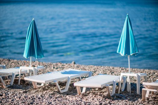 Several white sun loungers and a turquoise parasol on a deserted beach. The perfect vacation concept.