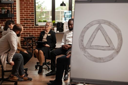Patients sitting in circle at group therapy program while having aa meeting symbol