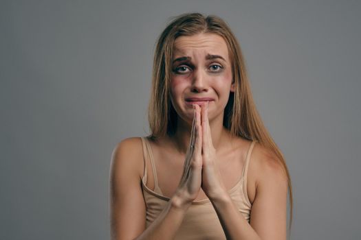 Blonde girl with bruises on her face, begging for mercy, posing against gray studio background. Domestic violence, abuse. Close-up, copy space.