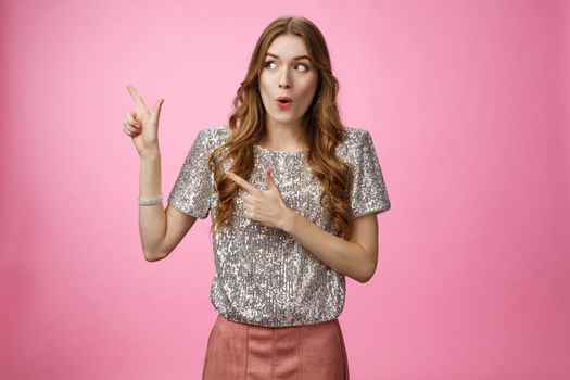 Wow interesting. Portrait amazed intrigued attractive young 20s girl shopping curious see cool promo folding lips widen eyes thrilled looking pointing left sideways, standing pink background