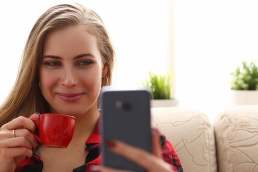 Young beautiful woman drinks coffee and looks into smartphone