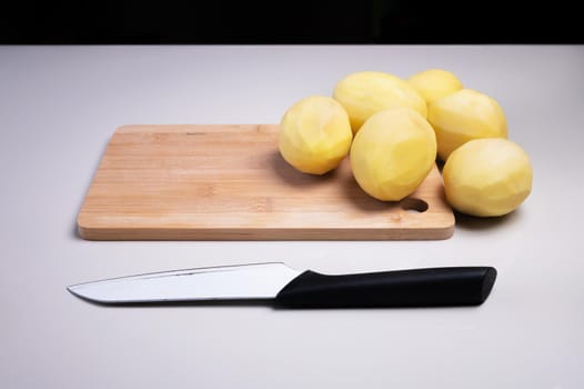 Peeled potatoes on a wooden cutting board next to a kitchen knife. Home cooking vegetables. Healthy food.