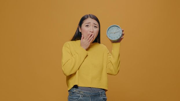 Asian woman with anxiety checking time on clock in studio