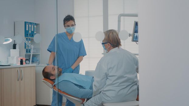 Orthodontist using dental tools to do teeth examination on patient with caries pain. Stomatologist and assistant analyzing procedure work after surgery with oral care instruments.