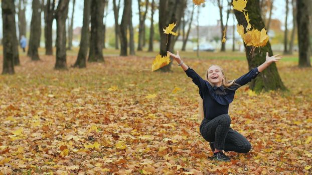 A young girl schoolgirl throws autumn leaves in a city park. Slow motion.