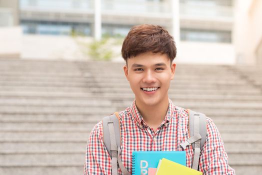 College asian male student holding book in campus