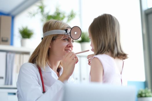 Woman pediatrician looks at the throat of a little girl