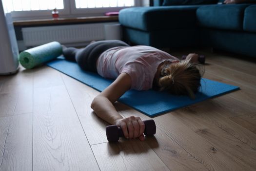 Exhausted sports woman with dumbbells lies on the floor