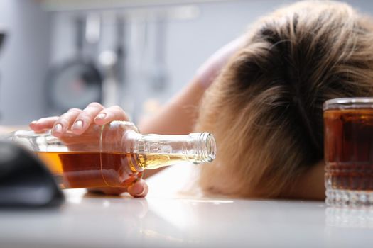 Drunk woman sleeping at the table a bottle of alcohol