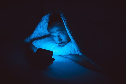 Young man lying in bed and using smartphone before sleep. Social media addiction and insomnia