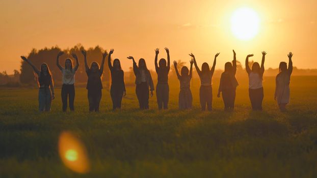 Silhouette of friends of 11 girls waving their hands at sunset in the field.