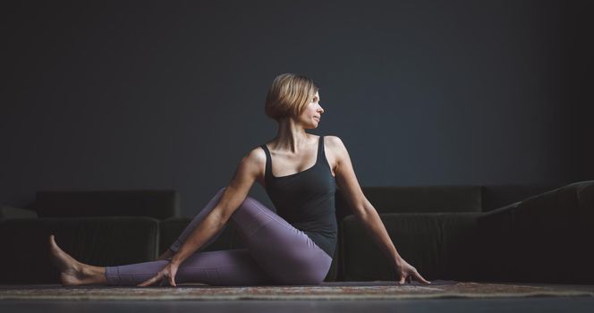 Yoga class. A beautiful, trained body. A woman makes an asana against a dark background in a city apartment. Body beauty concept. High quality photo