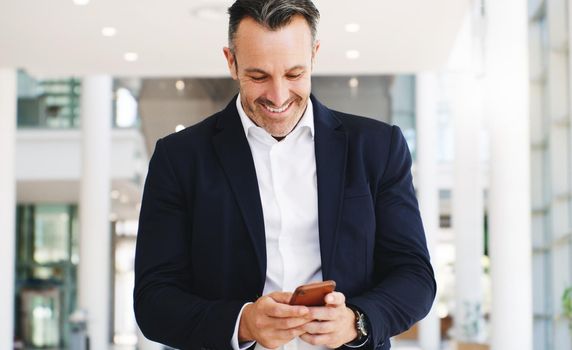 Instant connection brings instant good news. Shot of a mature businessman using a smartphone while walking through a modern office.