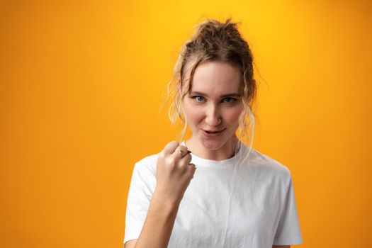 Portrait of furious and angry woman showing fist against yellow background