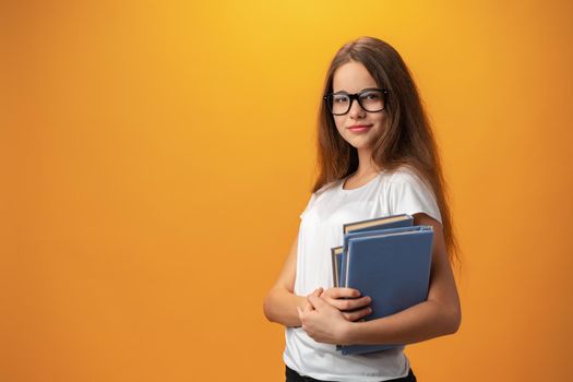 Smart teen girl in glasses holding book against yellow background