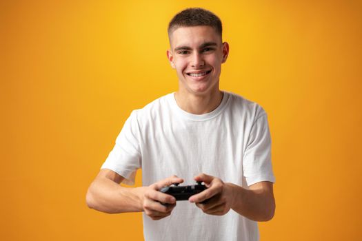 Young man playing computer games with jojystick against yellow background