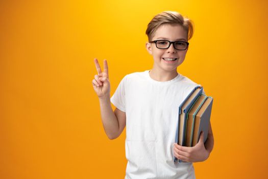 Little schoolboy holding a book against yellow background