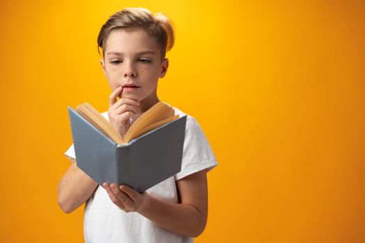 Little schoolboy holding a book against yellow background