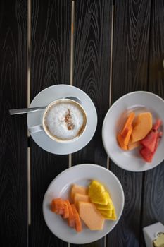 Delicious cup of latte and sliced fruit for breakfast on black table