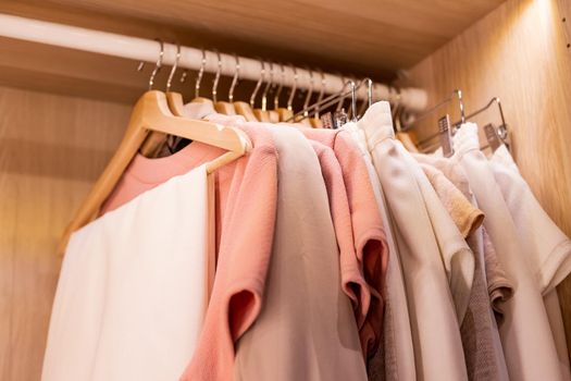 Hangers with different clothes in wardrobe closet.shirts and dress hanging on rail in wooden wardrobe. minimalistic modern scandinavian white wood walk in closet with wardrobe in neutral beige colors