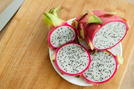 Slices of dragon fruit or pitaya with pink skin and white pulp with black seeds on white plate on the kitchen. Exotic fruits, healthy eating concept
