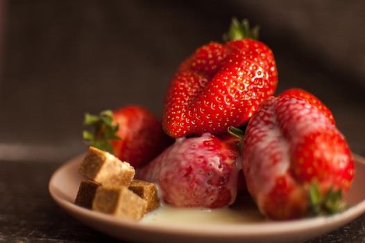 Red ripe strawberries on round plate with a few cane sugar pieces and melted white chocolate