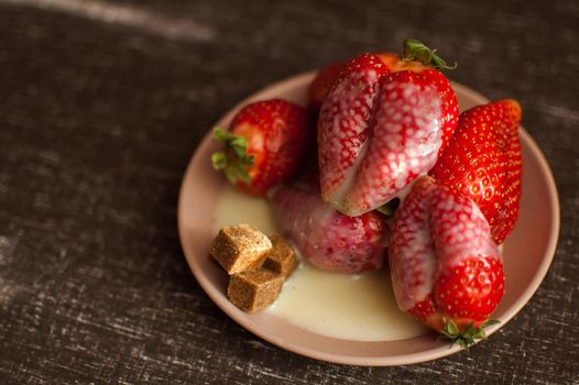Red ripe strawberries on round plate with a few cane sugar pieces and melted white chocolate