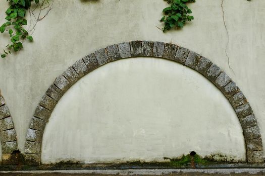 A walled door with a stone arch e against the background of an old beige plastered wall, photo frame, text place