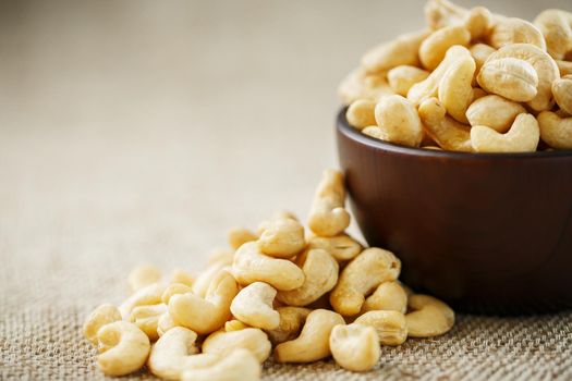 Cashew nuts in a wooden bowl on a burlap cloth background.