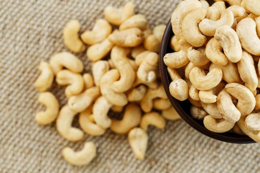 Cashew nuts in a wooden bowl on a burlap cloth background.