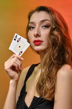 Brunette woman with earring in nose, in black dress. Showing two aces, posing on colorful background. Gambling, poker, casino. Close-up