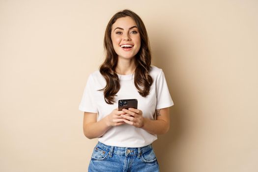 Happy modern woman smiling, holding smartphone and laughing, concept of cellular technology and mobile phone