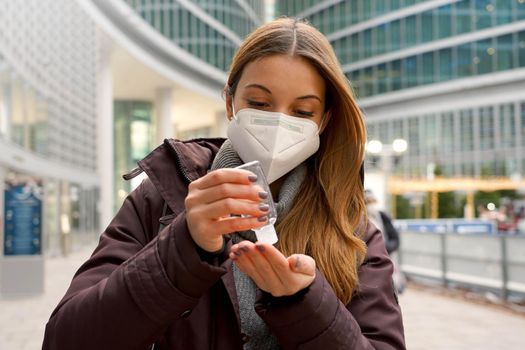 Young woman wearing protective medical mask using alcohol gel sanitizing her hands outside shopping mall. Hygiene and health care concept.