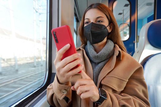 Girl in winter clothes wearing medical black mask on train using mobile phone