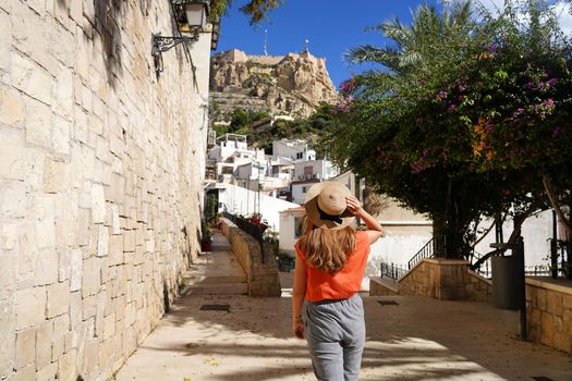 Exploring Alicante in Spain. Young traveler woman walking in the neighborhood Santa Cruz looking at Mount Benacantil with Santa Barbara castle in Alicante, Spain.