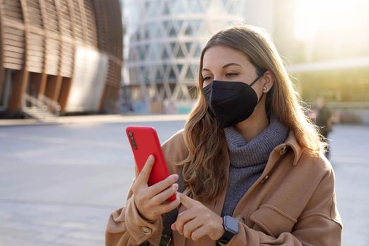 Young business woman wearing KN95 FFP2 mask using mobile phone app in city street
