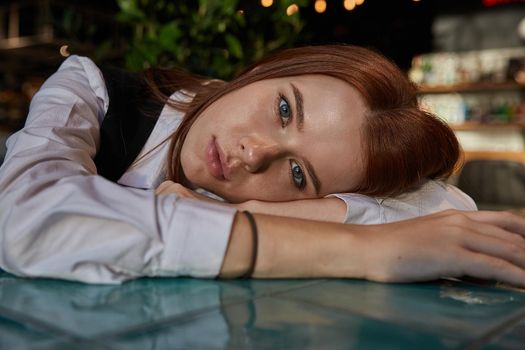 young redhead pretty girl with long hair lays her head on her arms and table