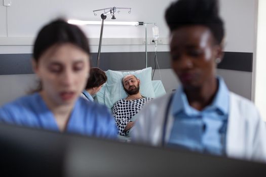 Doctor talking with admitted patient on hospital bed while nurse and resident looking at test results