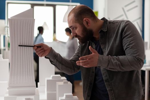 Engineer holding pen inspecting the design of skyscraper maquette