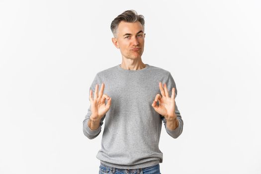 Image of impressed and satisfied middle-aged man, showing okay signs and nodding in approval, praise good choice, standing over white background
