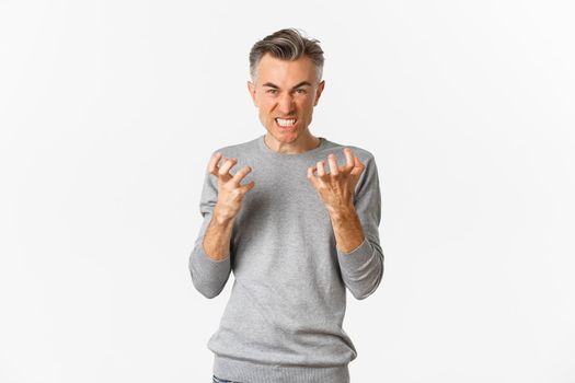 Image of angry middle-aged man cursing someone, looking mad and clenching fists with hatred, standing over white background