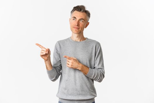 Image of thoughtful middle-aged man making choice, looking and pointing left, standing over white background
