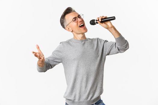 Portrait of passionate middle-aged man singing serenade in microphone, standing carefree over white background