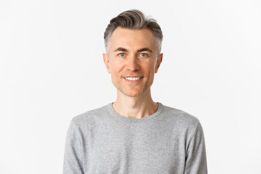 Close-up of handsome middle-aged man in gray sweater, looking happy and hopeful, smiling at camera, standing over white background