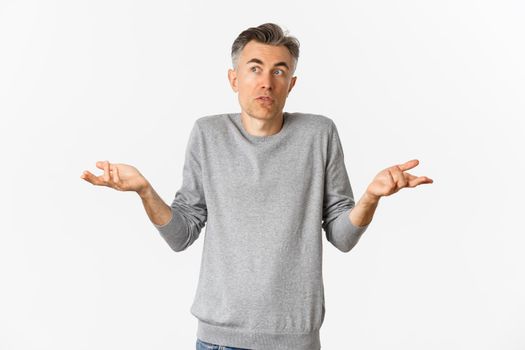Image of confused middle-aged man with grey hair, shrugging and looking away, cannot understand something, standing over white background