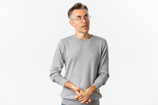 Image of annoyed middle-aged man rolling eyes, looking up, wearing sweater and glasses, standing over white background