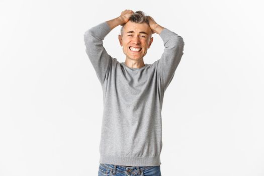 Image of frustrated middle-aged man panicking, losing something, ripping hair on head and grimacing from distress and failure, standing over white background