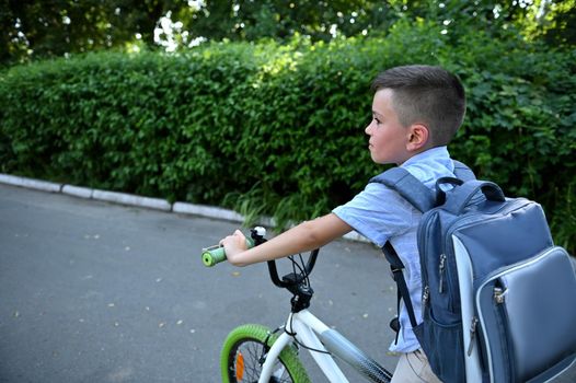 Handsome schoolboy biking to school on asphalt road.