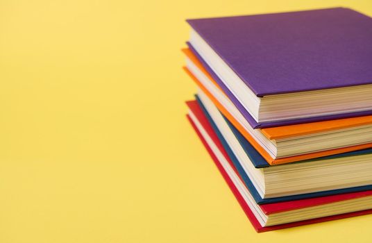 Stack of multicolored books on yellow surface background with copy space for text. Teacher's Day concept, Knowledge, literature ,reading, erudition